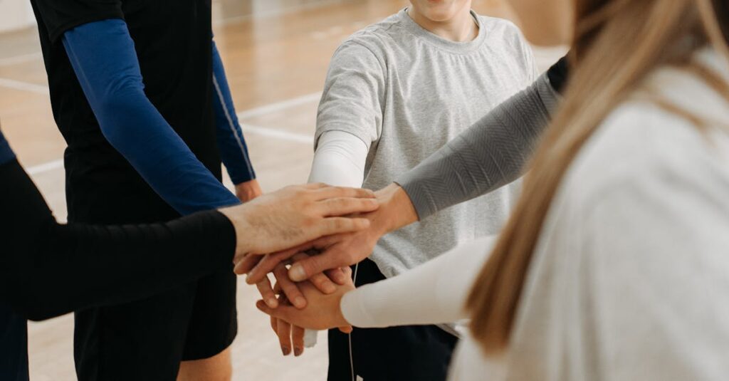Group of young athletes joining hands in a gym, symbolizing teamwork and unity.