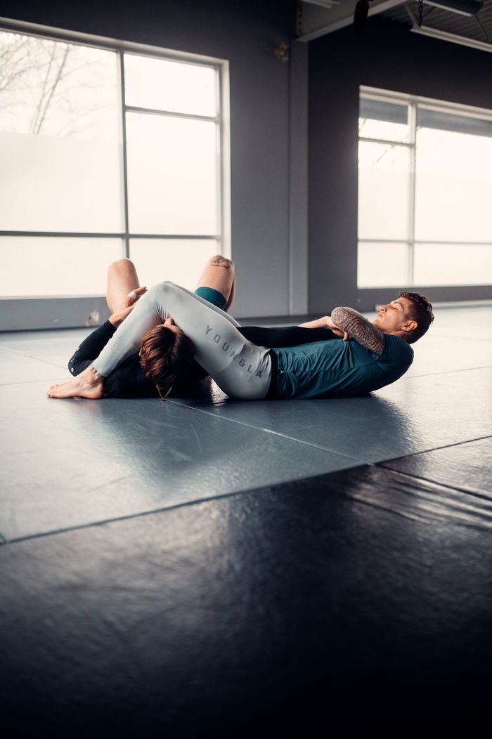 Two people practicing martial arts grappling on a gym mat indoors.